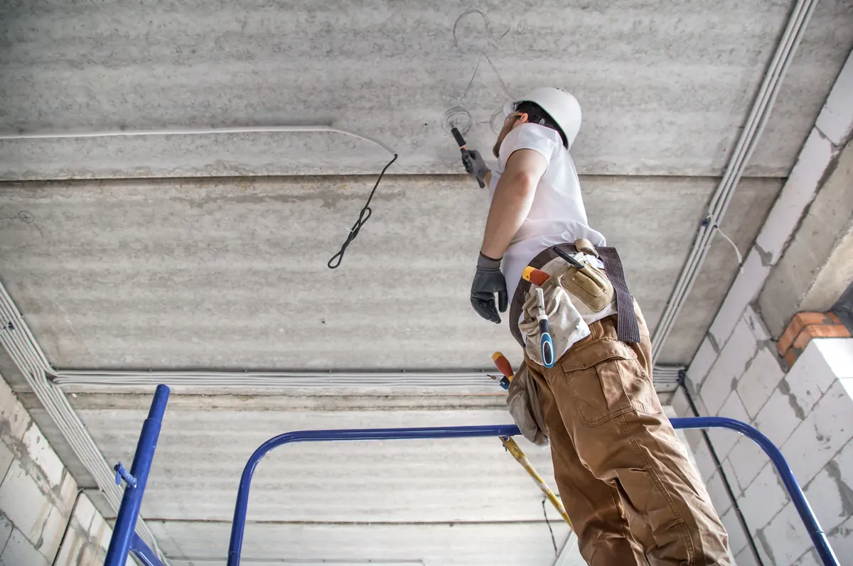 Electrician on a ladder working at a ceiling inside a building