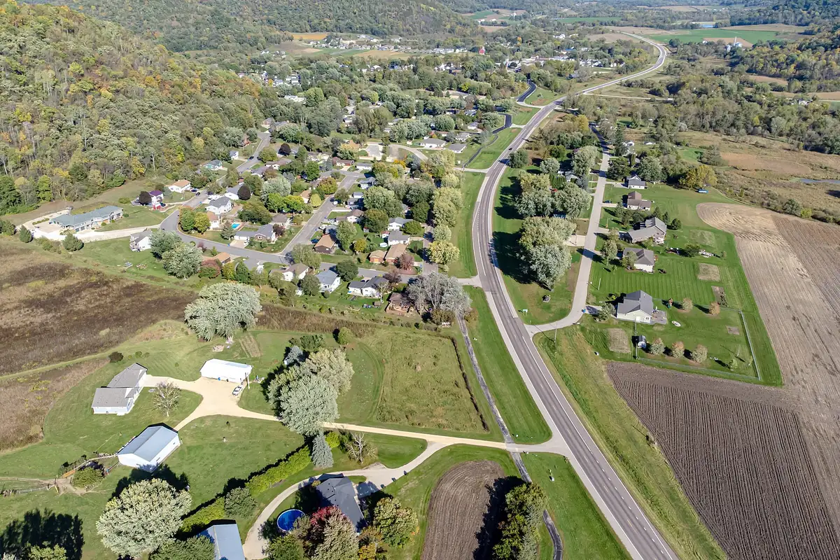 Aerial view of Rollingstone, Minnesota, with homes along a highway in a valley of autumn-coloured woods.