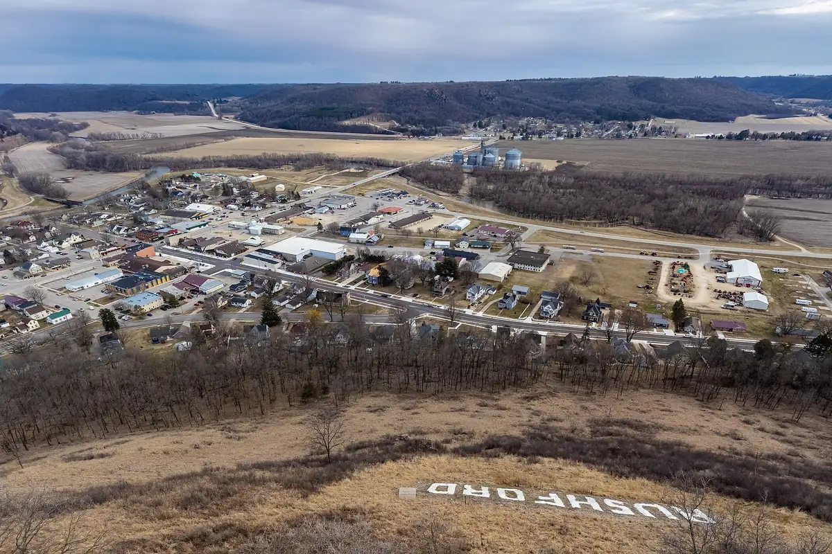 View from the bluff over Rushford, Minnesota, with the town below, river valley beyond and the town name in large letters on the hillside.